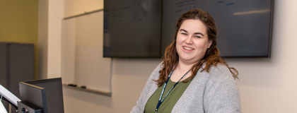 MCC Instructor Cheyenne Beach standing behind a desk wearing a green shirt and gray cardigan and smiling.