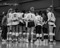 Black and white photo of the women's volleyball team standing on the court with their arms around eachother in a huddle.