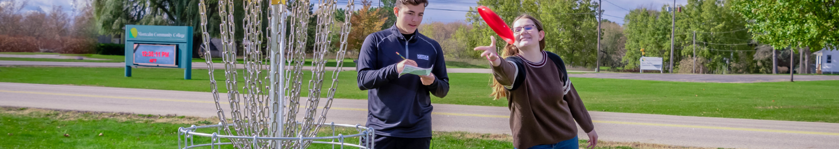 Male and female students toss disc into disc golf bin