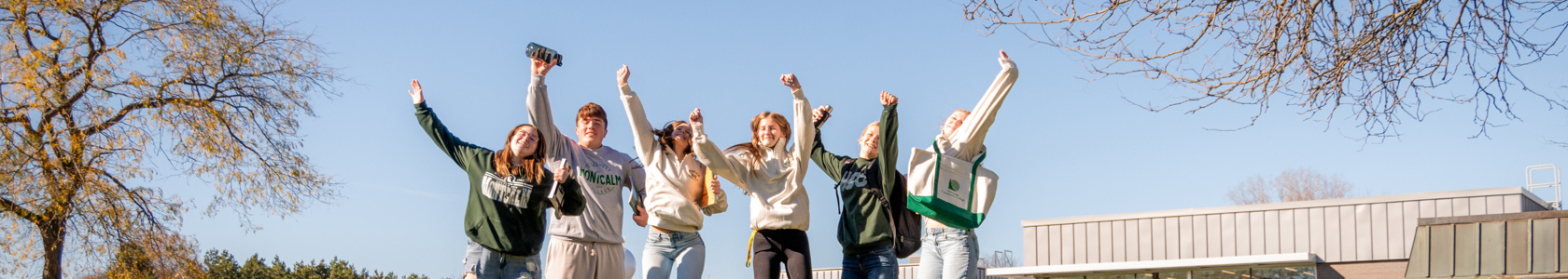 Six students outside on MCC's Sidney campus jumping in the air excitedly.