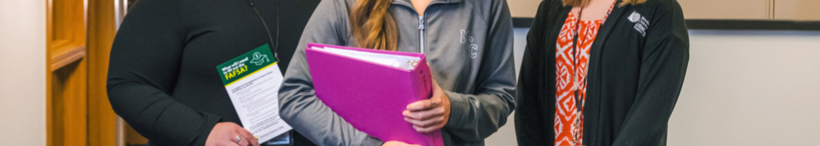 student with pink binder standing in front of two financial aid advisors