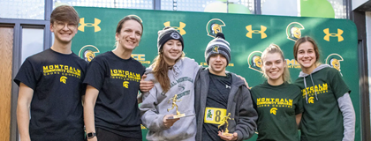 Centurion 5K runners pose in front of the MCC Athletics backdrop with their trophies. Photo courtesy of the Daily News.