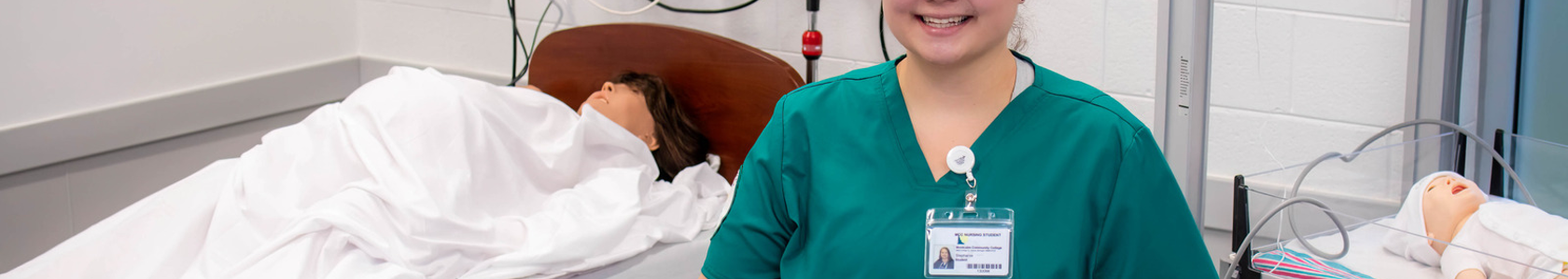 Student in green scrubs in nursing simulation lab.