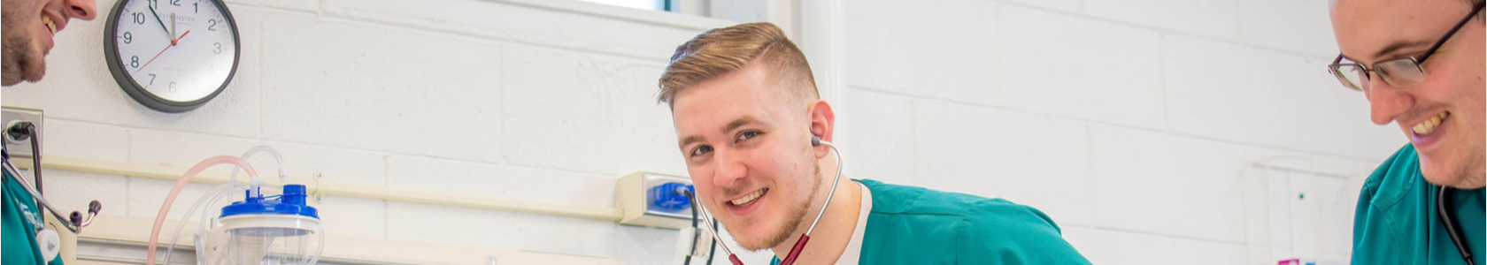 Male nursing student in green scrubs using stethoscope in simulation lab.