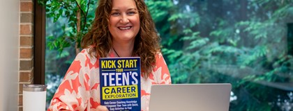 Career Services Advisor, Amy Zdanowski, holding her published book "Kick Start Your Teen's Career Exploration" at a desk.