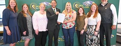MCC staff and Carson City-Crystal schools staff pose in front of a backdrop featuring both schools logos with a paper copy of the new direct admissions agreement.