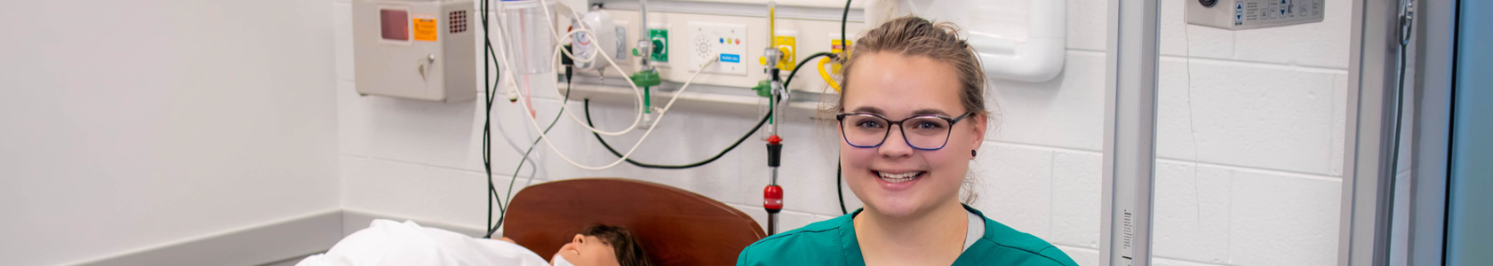 Female Nursing Student smiling in front of hospital bed.