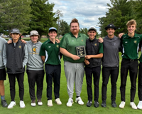 Team photo of the 25-26 men's golf team standing on a course holding up a plaque.