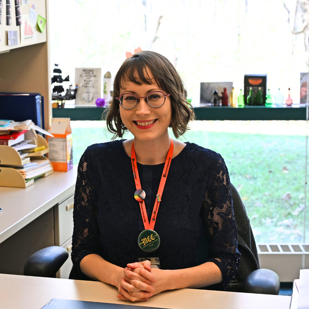 MCC Instructor Andrea Martin sitting at her desk with hands clasped and smiling.